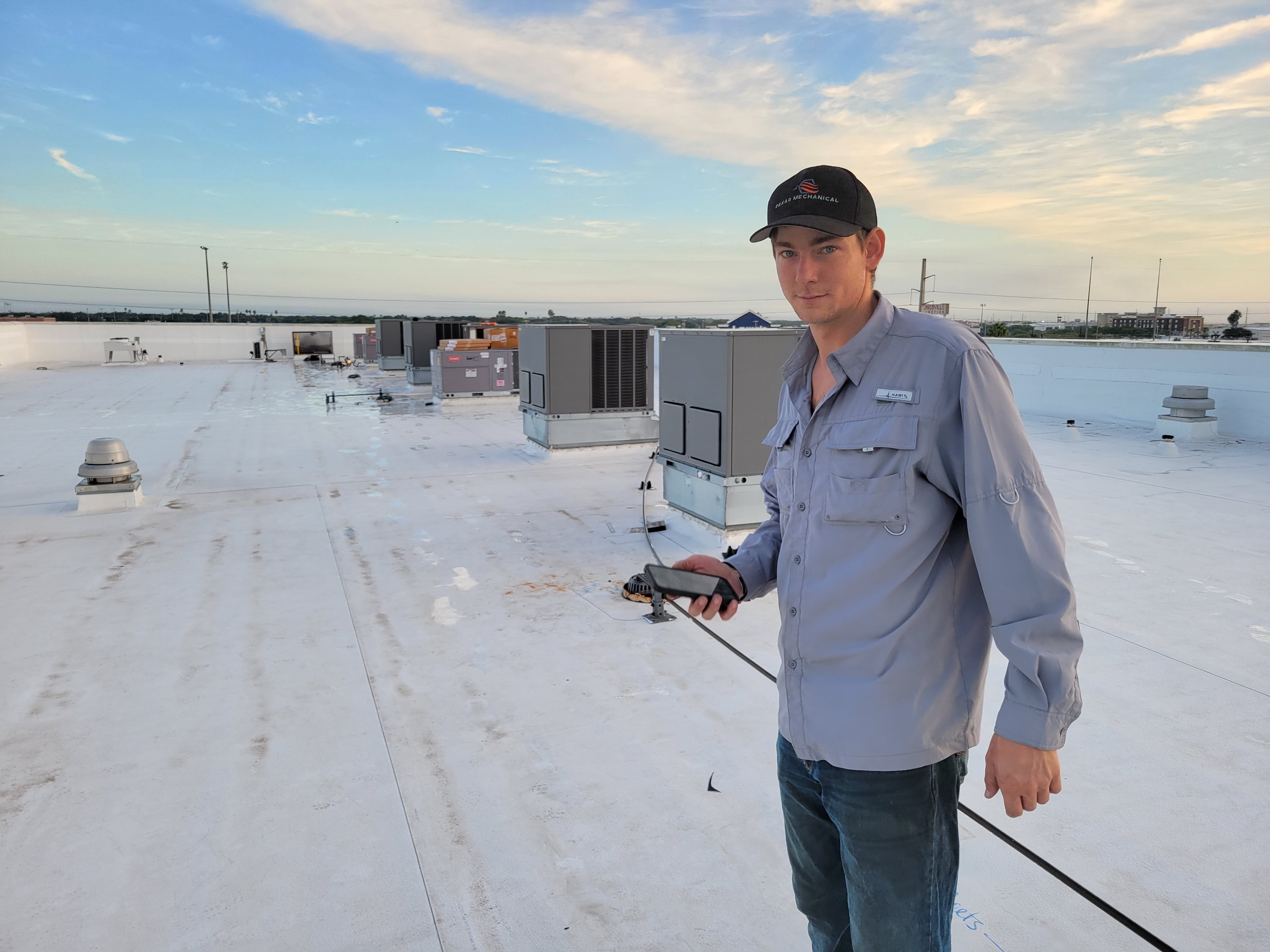 Technician servicing a rooftop HVAC unit with city skyline in background